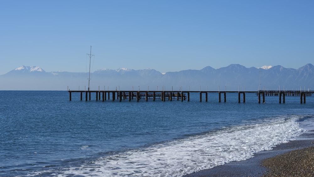 a pier on a beach with mountains in the background
