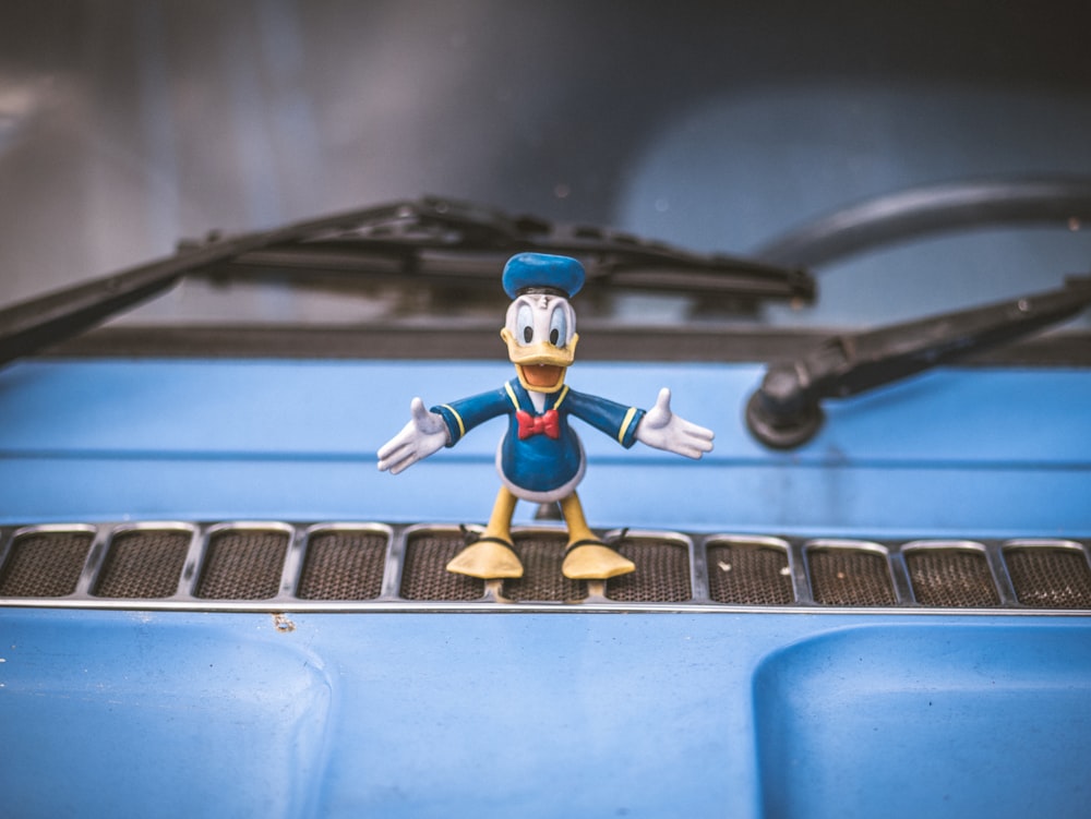 a mickey mouse figurine sitting on the hood of a car