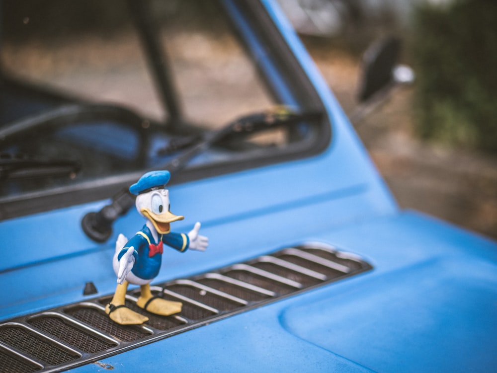 a toy duck is standing on the hood of a car