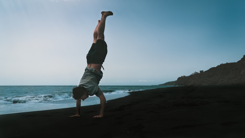 a man doing a handstand on the beach