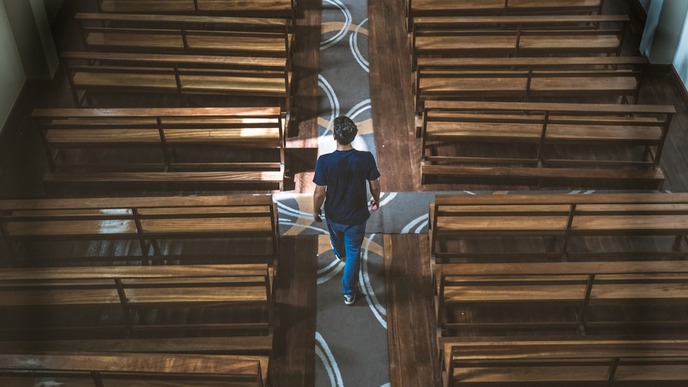 a man walking down a hallway between wooden benches