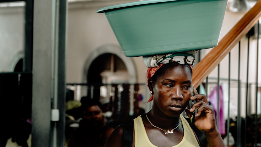 a woman with a bucket on her head talking on a cell phone