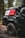 A rugged, off-road vehicle with the logo 'TRD 4x4 Sport' is parked in a forest setting. The vehicle is equipped with large, all-terrain tires and carries camping and off-road gear on its roof rack, including red and white fuel canisters and a black cargo bag labeled '23ZERO'. The trees and dirt road suggest a remote, adventurous location.