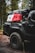 A rugged, off-road vehicle with the logo 'TRD 4x4 Sport' is parked in a forest setting. The vehicle is equipped with large, all-terrain tires and carries camping and off-road gear on its roof rack, including red and white fuel canisters and a black cargo bag labeled '23ZERO'. The trees and dirt road suggest a remote, adventurous location.
