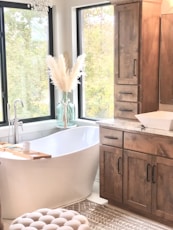 a bathroom with a tub, sink, cabinets and a window