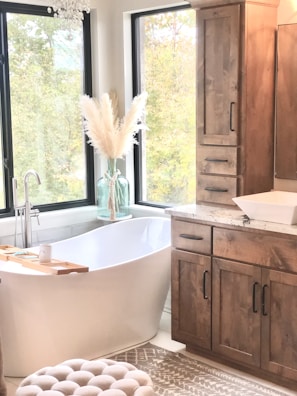 a bathroom with a tub, sink, cabinets and a window