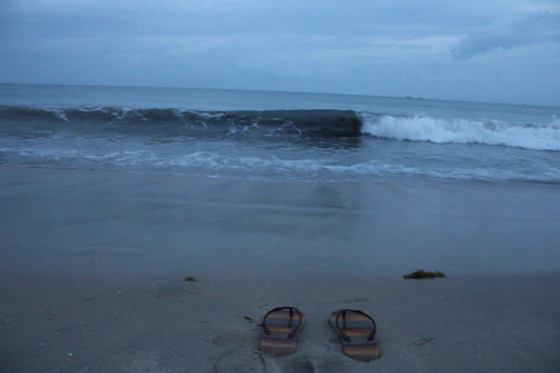 A serene beach scene with sandals resting on soft sand near gentle waves.