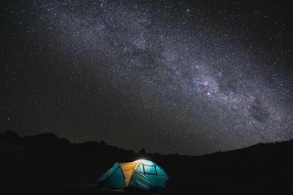 a tent pitched up in the middle of a field under a night sky filled with