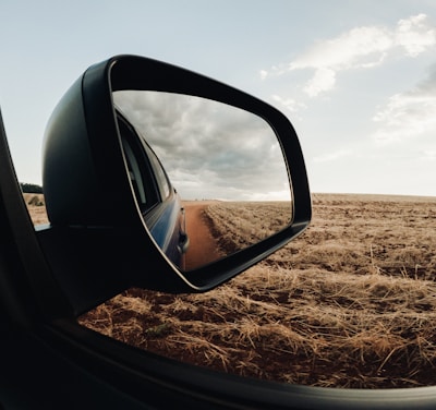 a rear view mirror of a car on a dirt road