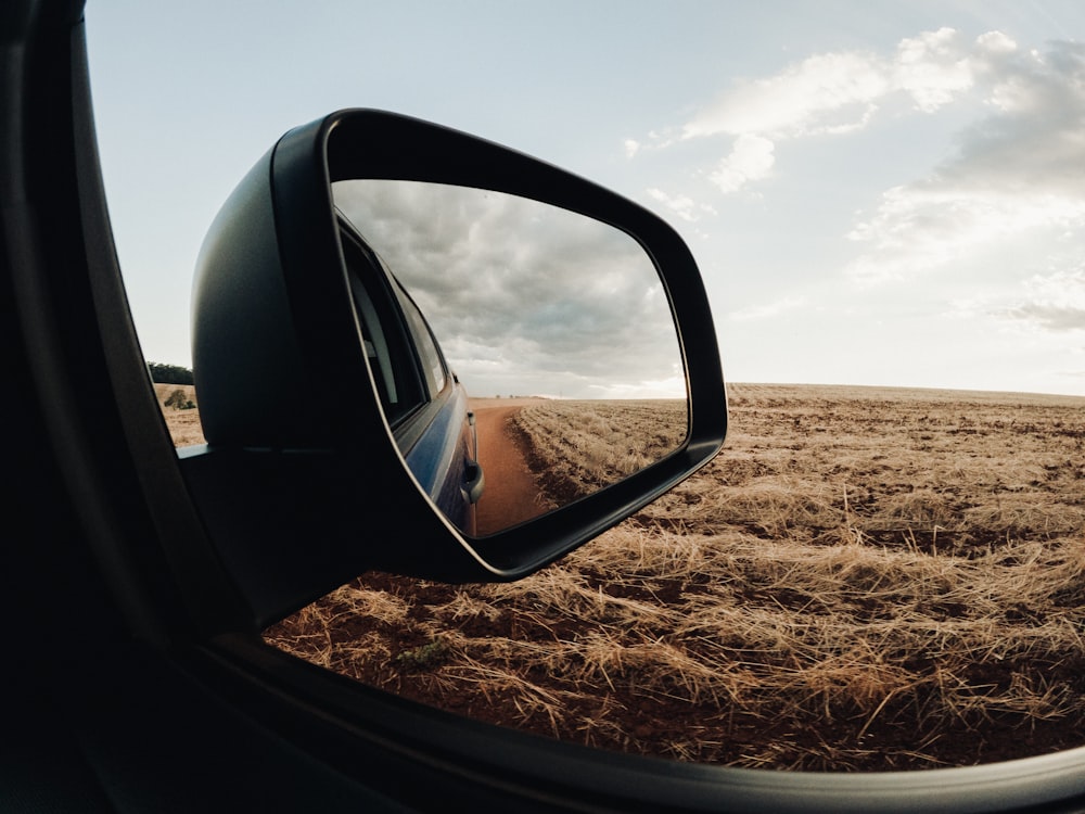 a rear view mirror of a car on a dirt road