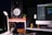 A well-organized workspace featuring an audio studio setup including a large speaker, a modern desktop computer displaying audio editing software, a pair of headphones resting on a stand, and a small potted plant for decor. The setup is illuminated by a sleek desk lamp, creating a warm, inviting atmosphere. Decorative owl figures also add a touch of personality to the space.