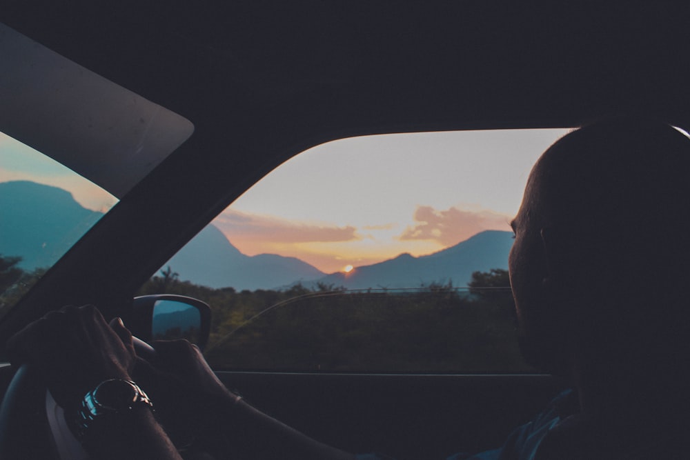 a man driving a car at sunset with mountains in the background