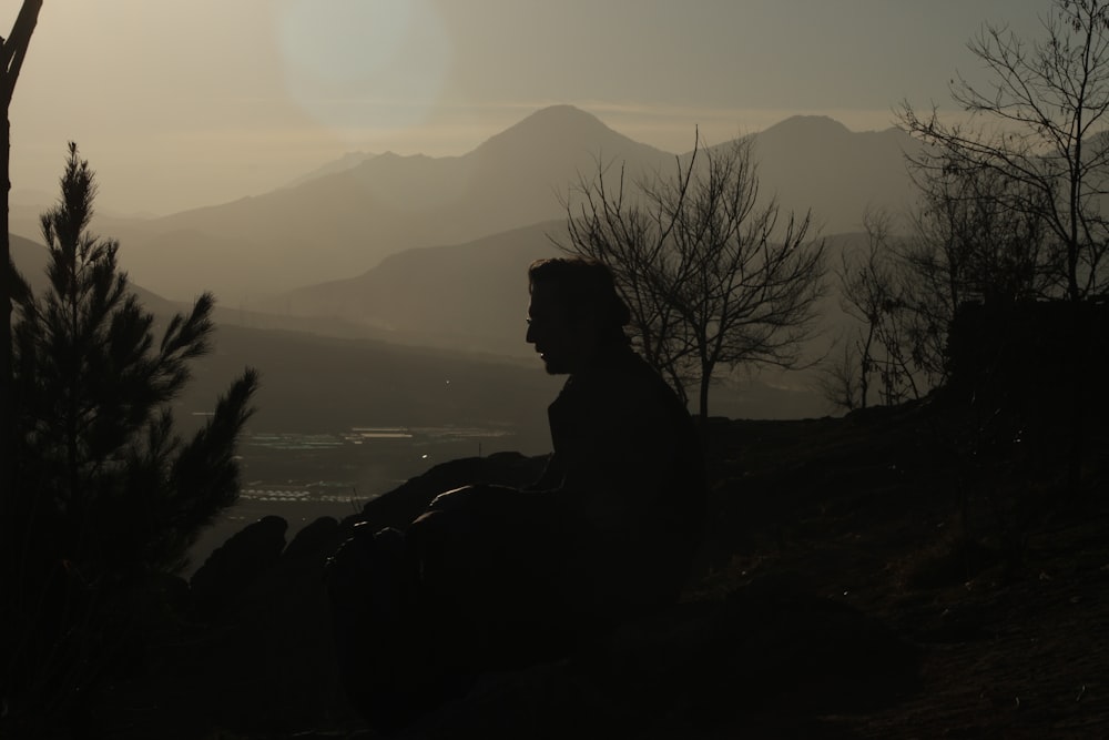 Una silhouette di un uomo seduto sulla cima di una collina