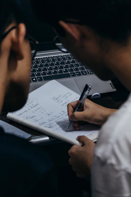 a man writing on a piece of paper next to a laptop