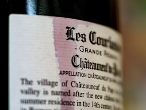 Close-up of a wine bottle label with text in ornate font and some blurred text in the background. The label features names such as 'Les Courriers' and 'Châteauneuf du Pape'. The design suggests a vintage or traditional style.