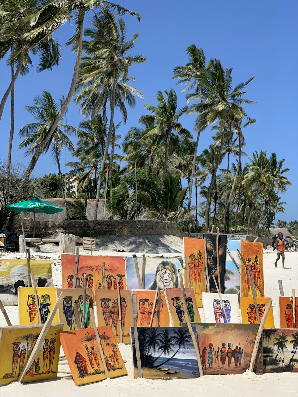 a number of paintings on a beach near palm trees