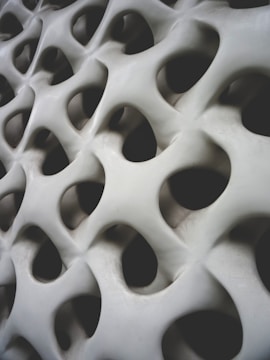 Organic, three-dimensional surface with smooth, flowing curves and multiple holes resembling a honeycomb or biological structure.