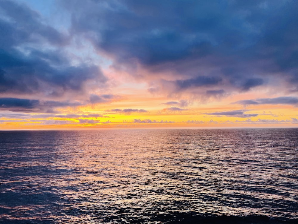 the sun is setting over the ocean on a cloudy day