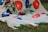 A piece of fabric with a floral design featuring vibrant red and blue flowers connected by green stems and leaves. The fabric is draped over grass, creating a natural backdrop that contrasts with the vivid colors of the textile.