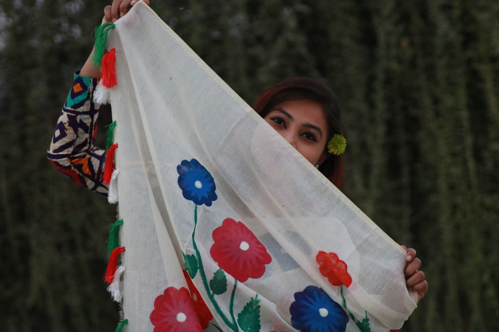 a woman holding a white scarf with flowers on it