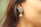 An ornate silver earring with a sunburst design is worn by a person. The earring features small intricate details and hangs delicately from the earlobe. The background is a soft color, focusing attention on the jewelry.