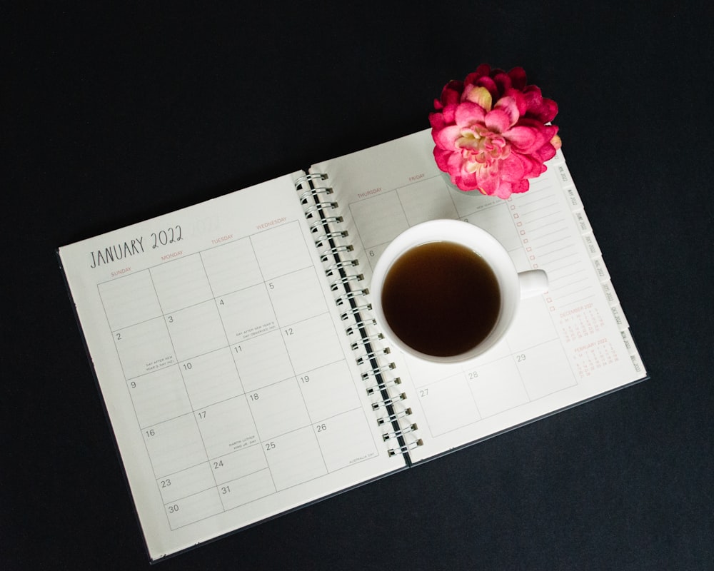 a cup of coffee sitting on top of a desk next to a calendar