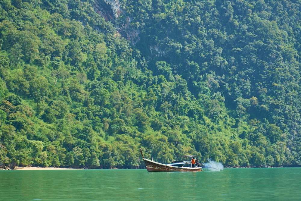 a boat floating on top of a lake next to a lush green hillside