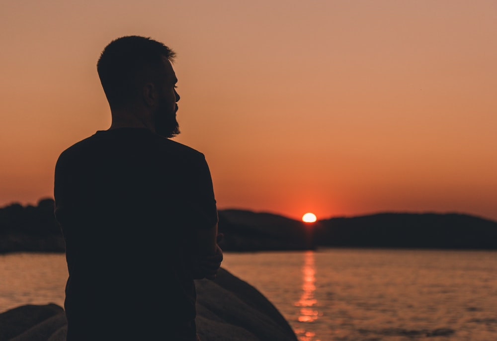 a man standing in front of a body of water at sunset