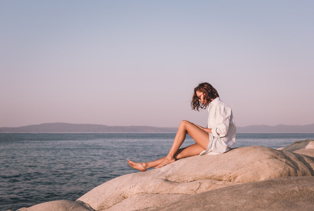 a woman sitting on top of a rock next to the ocean