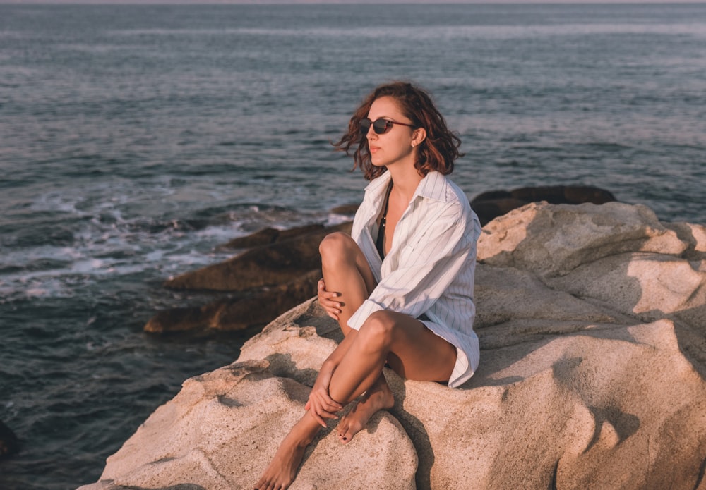 a woman sitting on top of a rock near the ocean