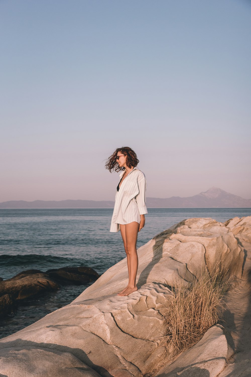 a woman standing on top of a rock near the ocean