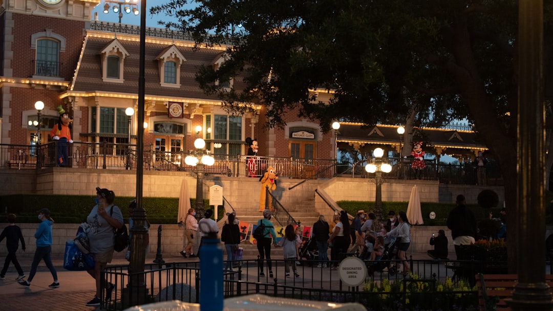 a crowd of people walking around a plaza at night, Costumed characters say goodbye at the gate at Disneyland, California in May 2021 (Covid)