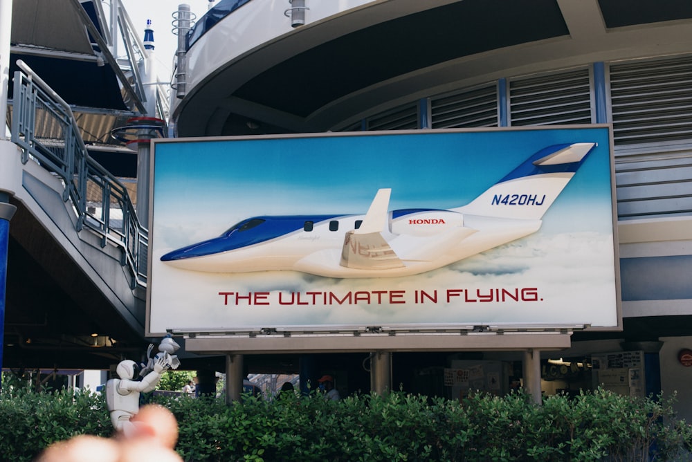 un cartellone pubblicitario con un aereo di fronte a un edificio