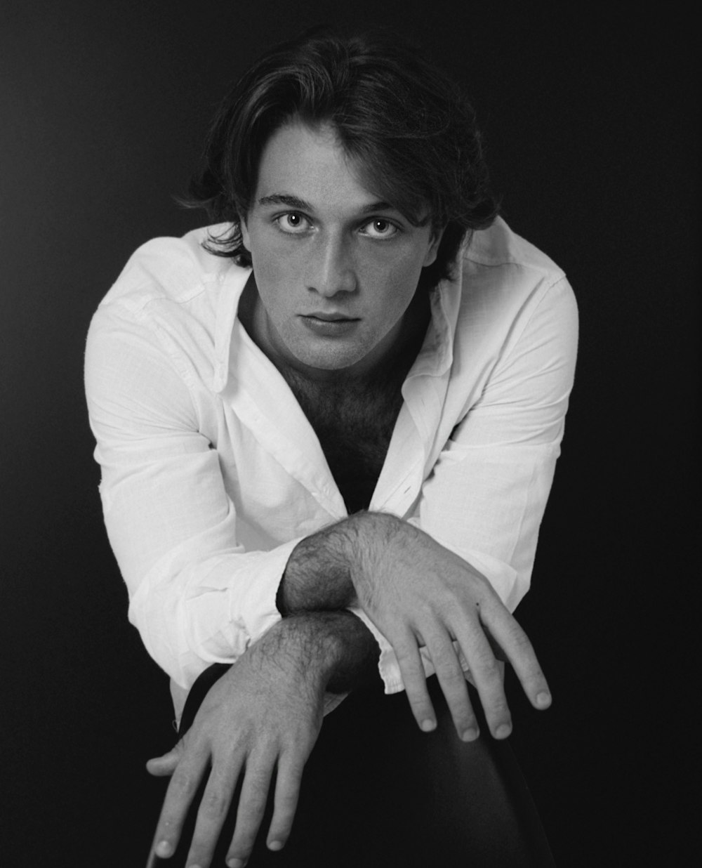 a black and white photo of a man leaning on a chair