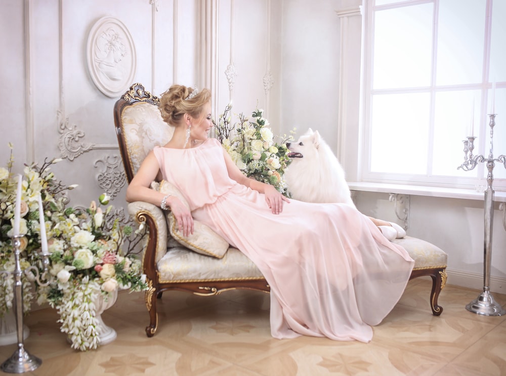 a woman in a pink dress sitting on a chair with a dog