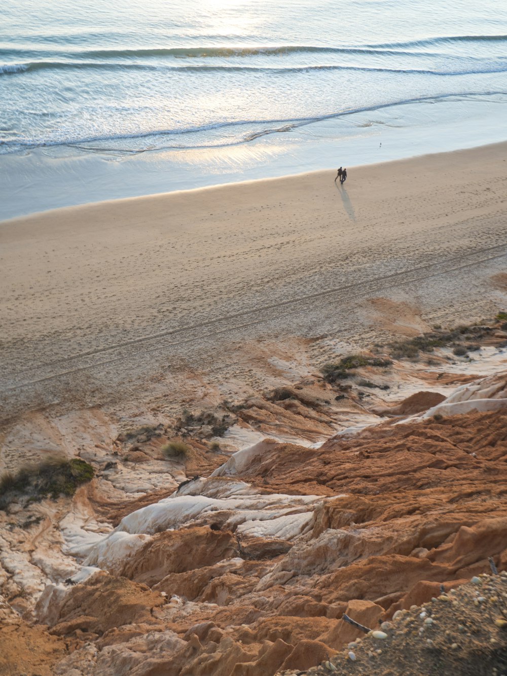 a couple of people walking along a sandy beach