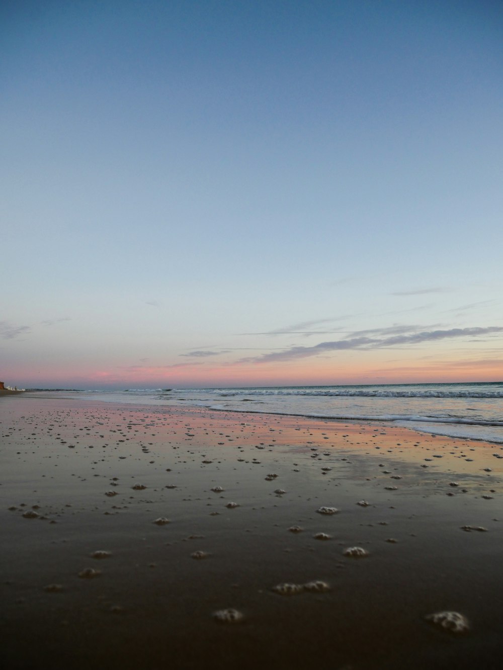 a beach with footprints in the sand and a lighthouse in the distance