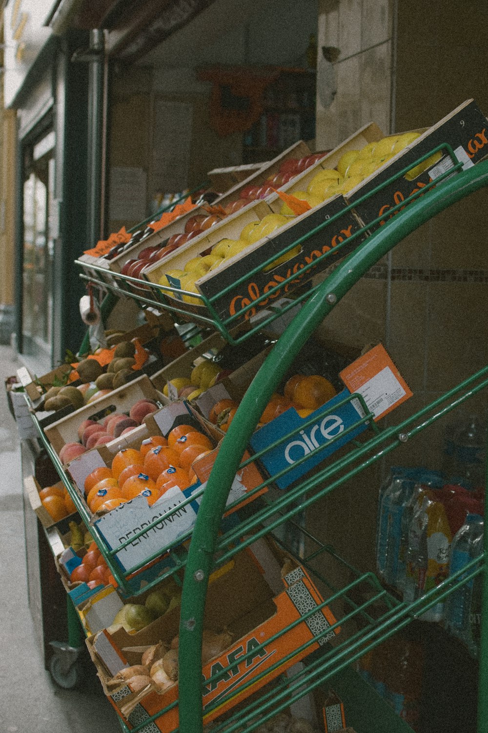 a green cart filled with lots of fruit next to a building