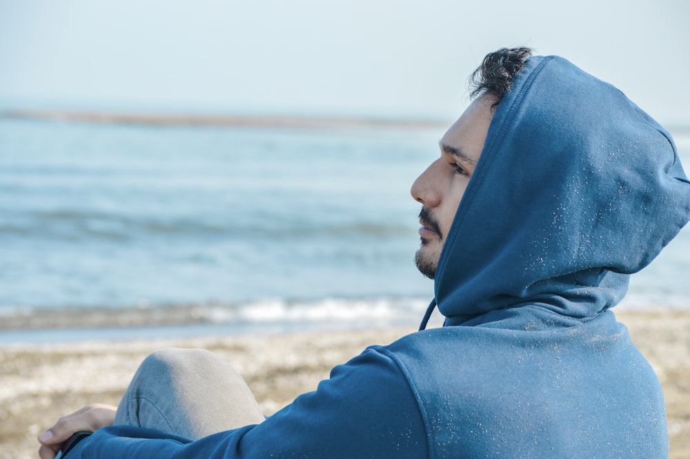 a man in a blue hoodie sitting on a beach