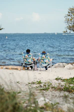 two people sitting in lawn chairs on a beach