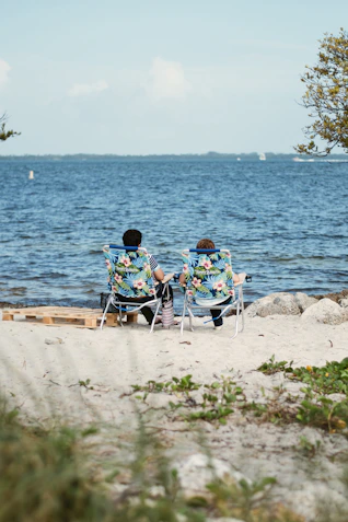 two people sitting in lawn chairs on a beach