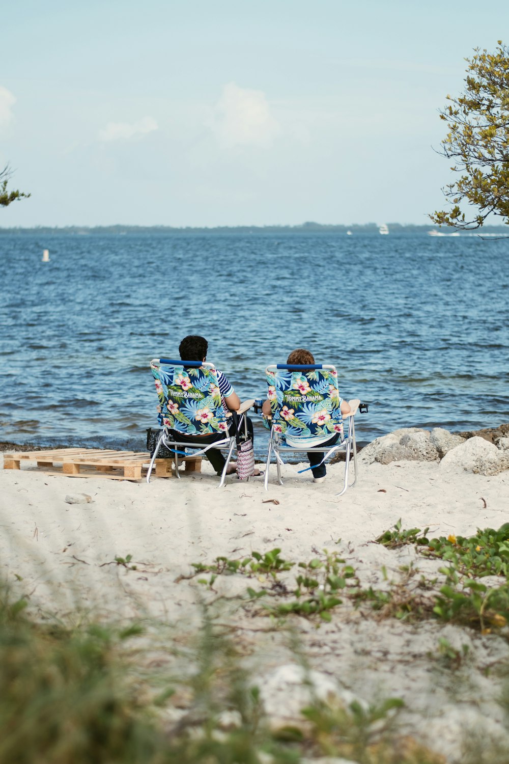 two people sitting in lawn chairs on a beach