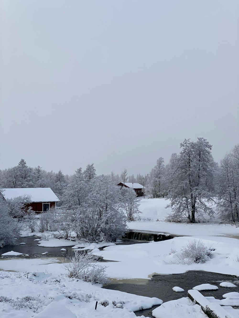 a snow covered landscape with a creek and a house