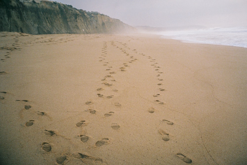 a beach with footprints in the sand and a cliff in the background