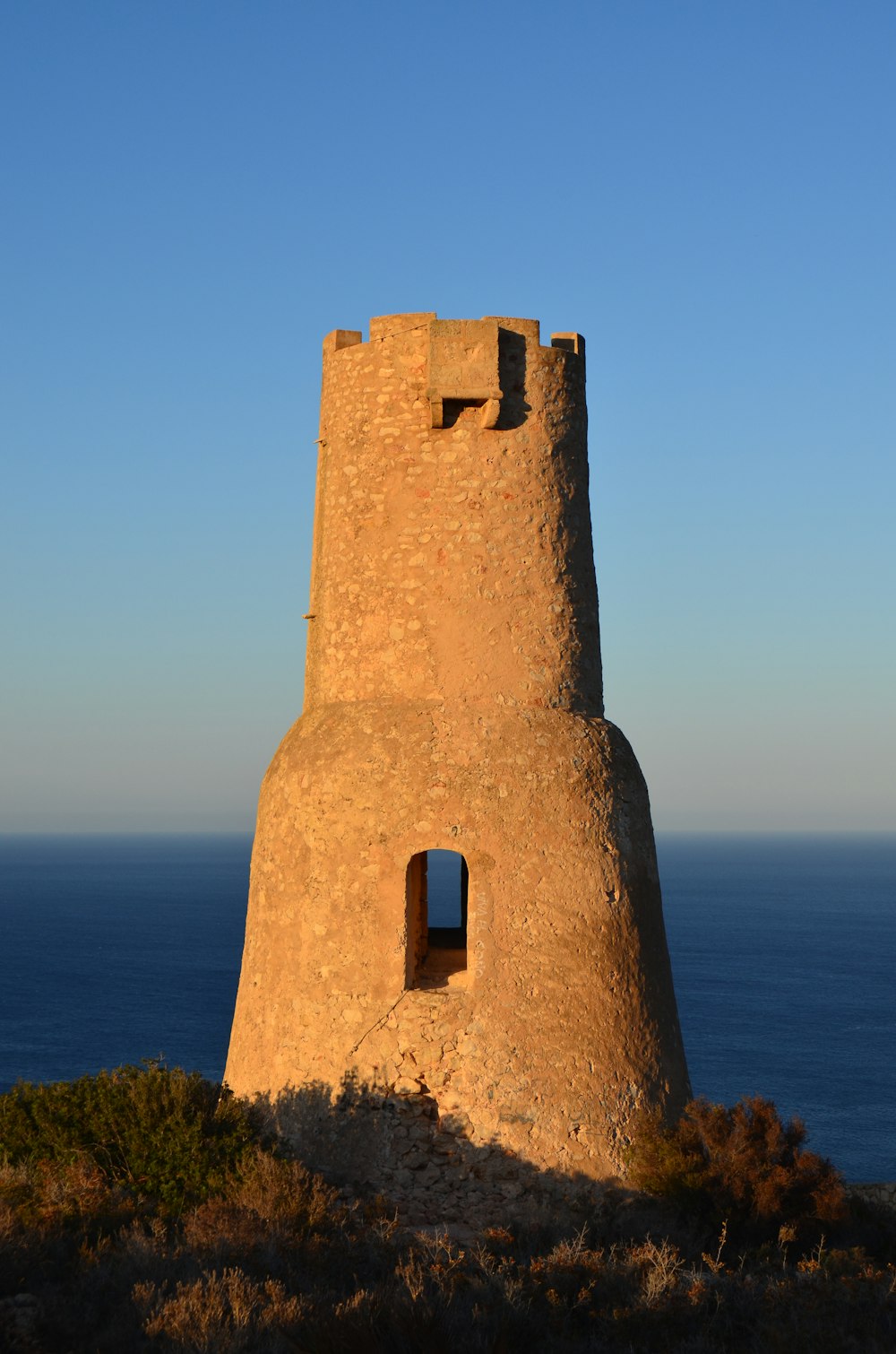 a stone tower sitting on top of a hill next to the ocean