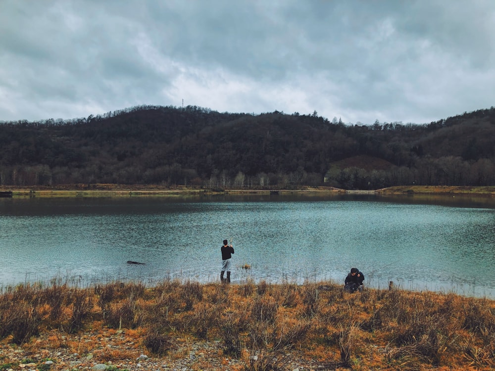 a man standing on top of a grass covered field next to a lake