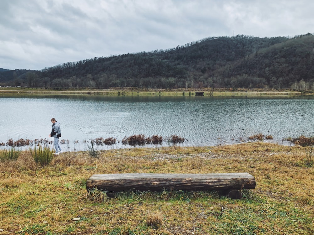 a man standing in front of a lake next to a log