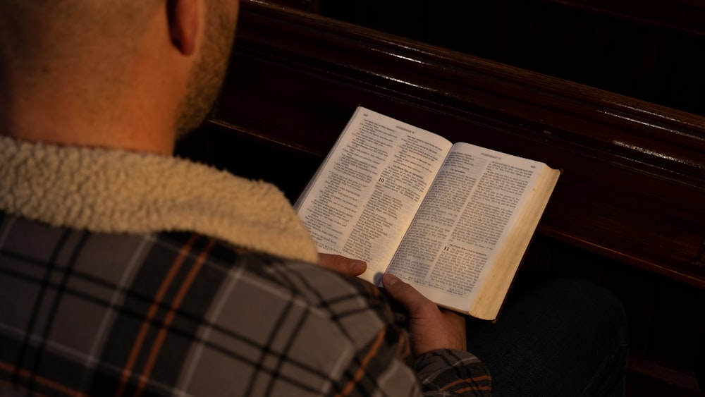 a man reading a book while sitting on a bench