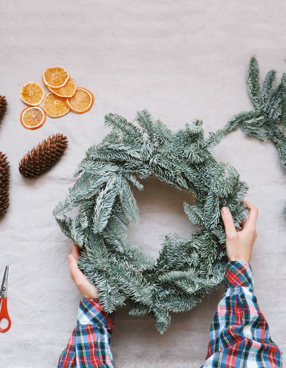 a person making a wreath with pine cones and oranges
