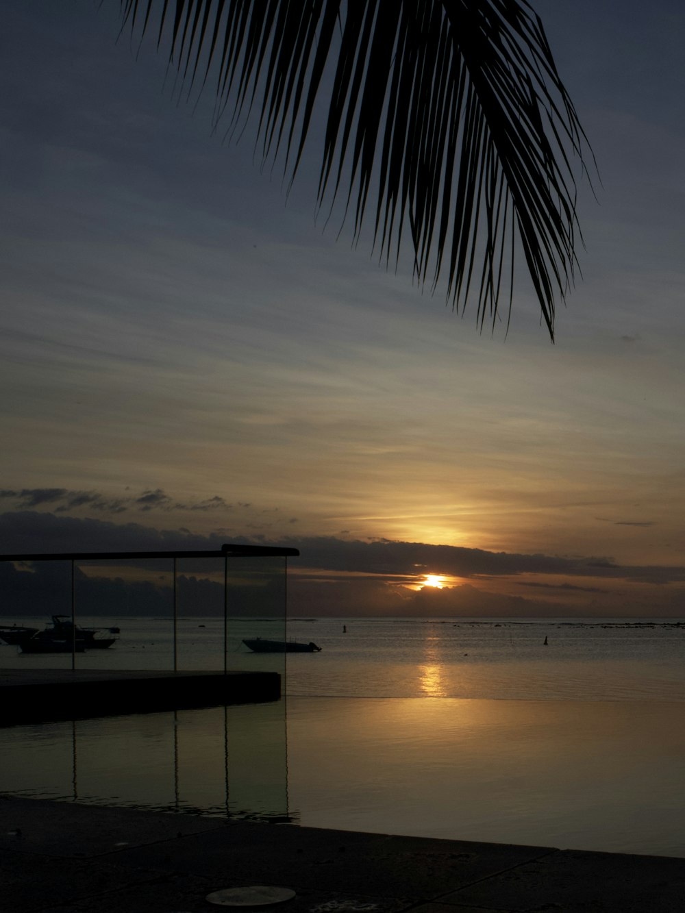 the sun is setting over the ocean with a boat in the water